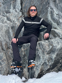  Person lying on rocky terrain with snow, wearing black athletic wear and sunglasses.