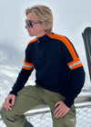 Man wearing Snow FInel Ski jumper sitting in the snow. Navy and orange