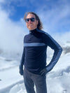 Person wearing a black and gray long-sleeve shirt with sunglasses and gloves, standing in a snowy landscape.