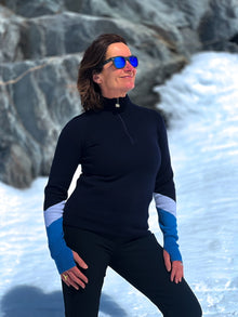  Person wearing a black long-sleeve top and blue gloves standing in a snowy landscape.